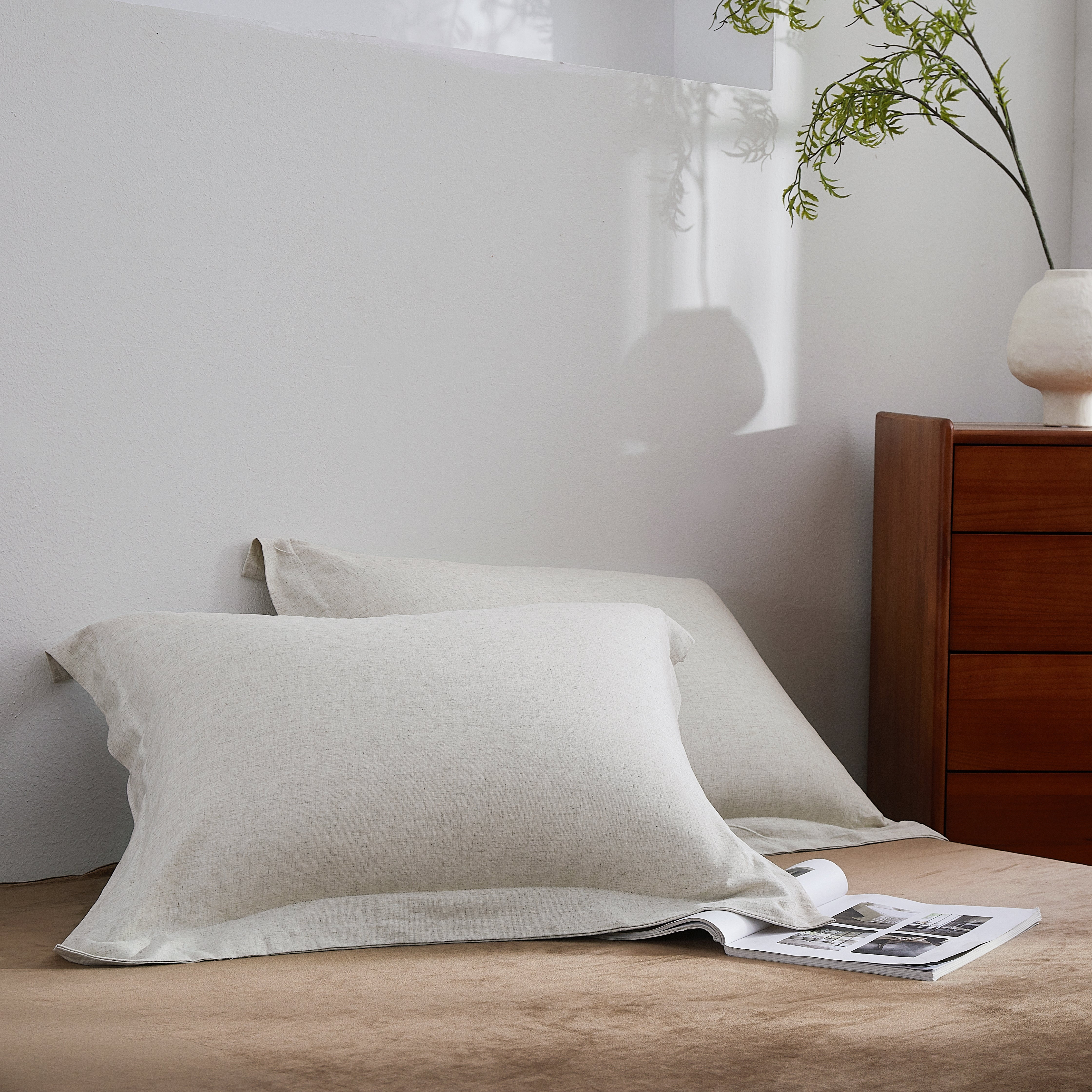 Beige pillows on a bed with a wooden nightstand and plant in the background