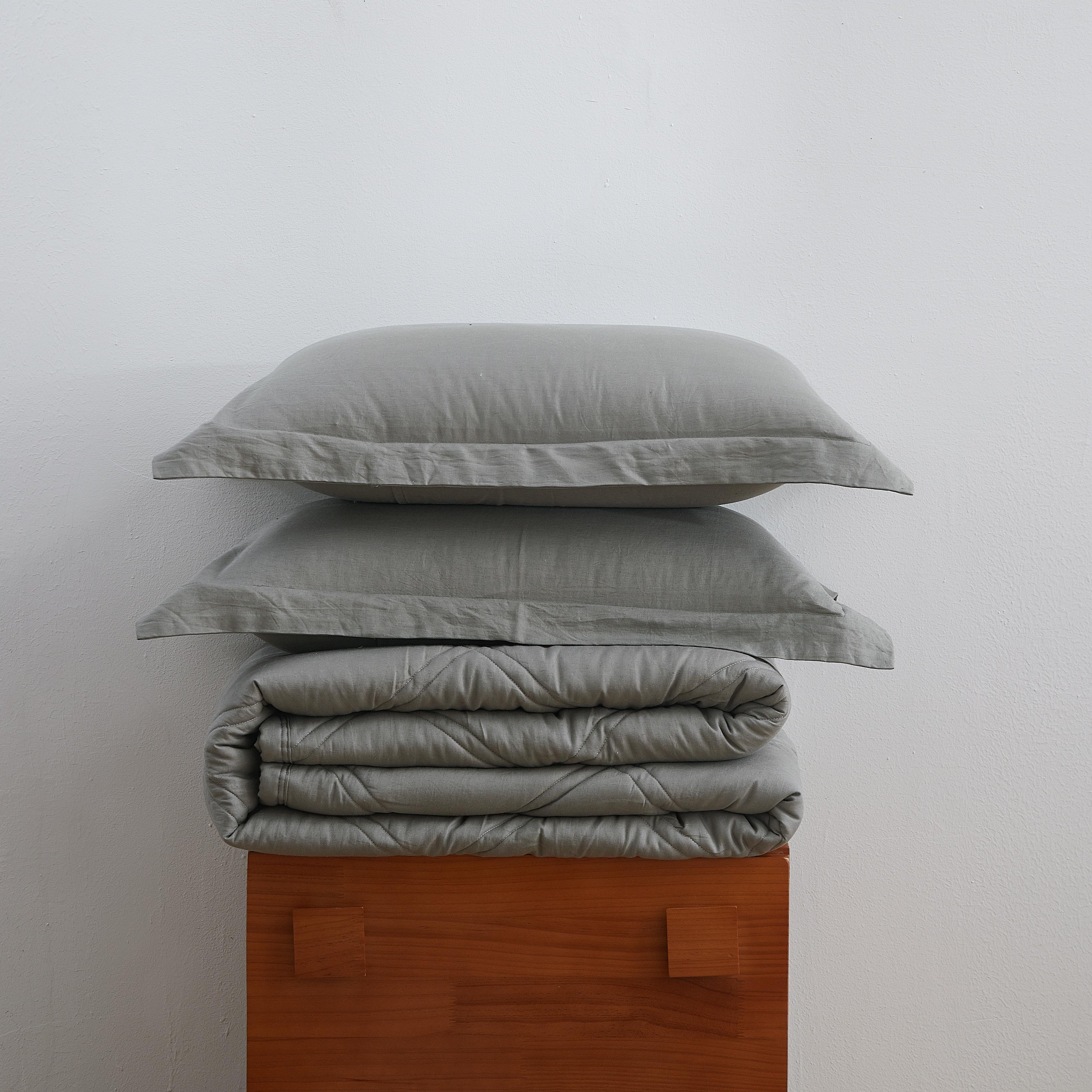 Stack of gray bedding on a wooden box against a white background