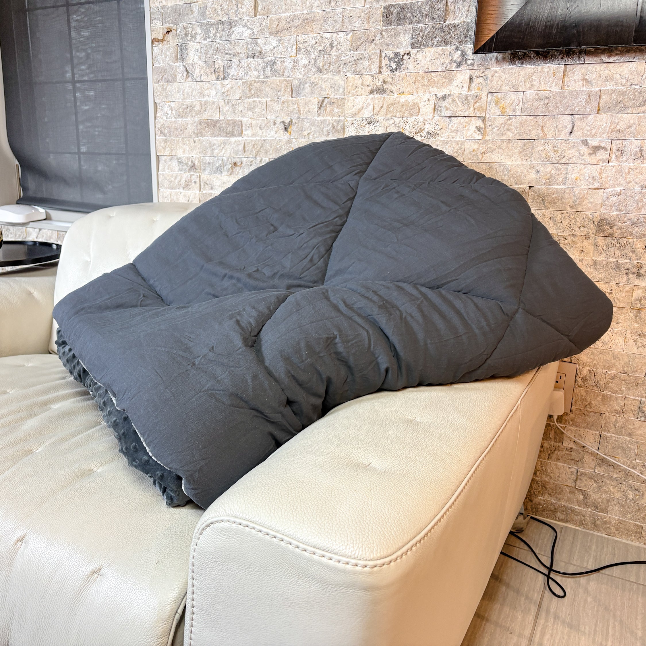 Gray cushion on a beige sofa against a stone wall.
