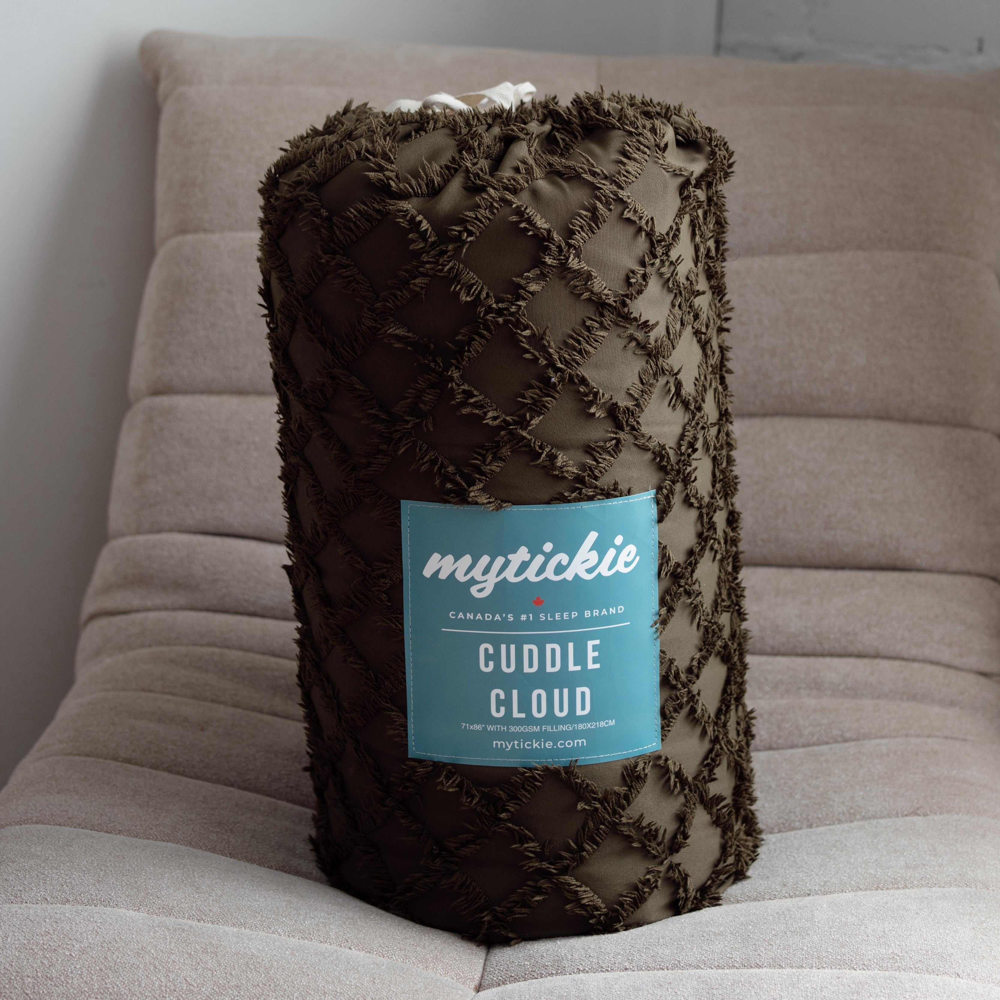 Fluffy Olive throw blanket with 'mytickle' label on a beige chair against a white brick wall.