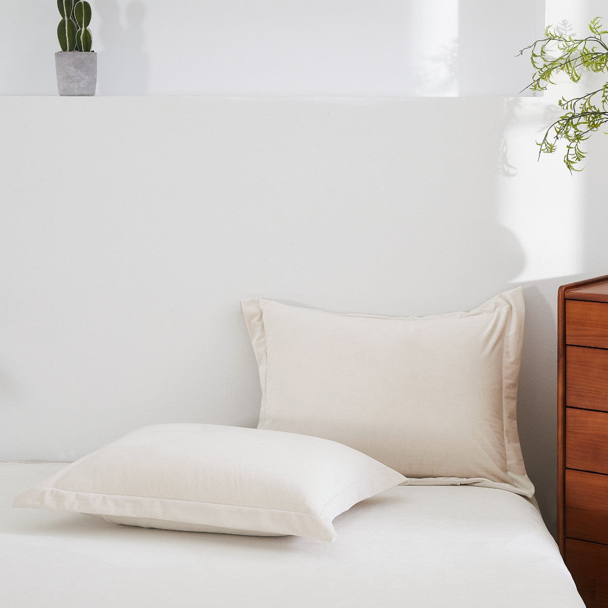 Beige pillows on a bed with a wooden nightstand and plants in the background