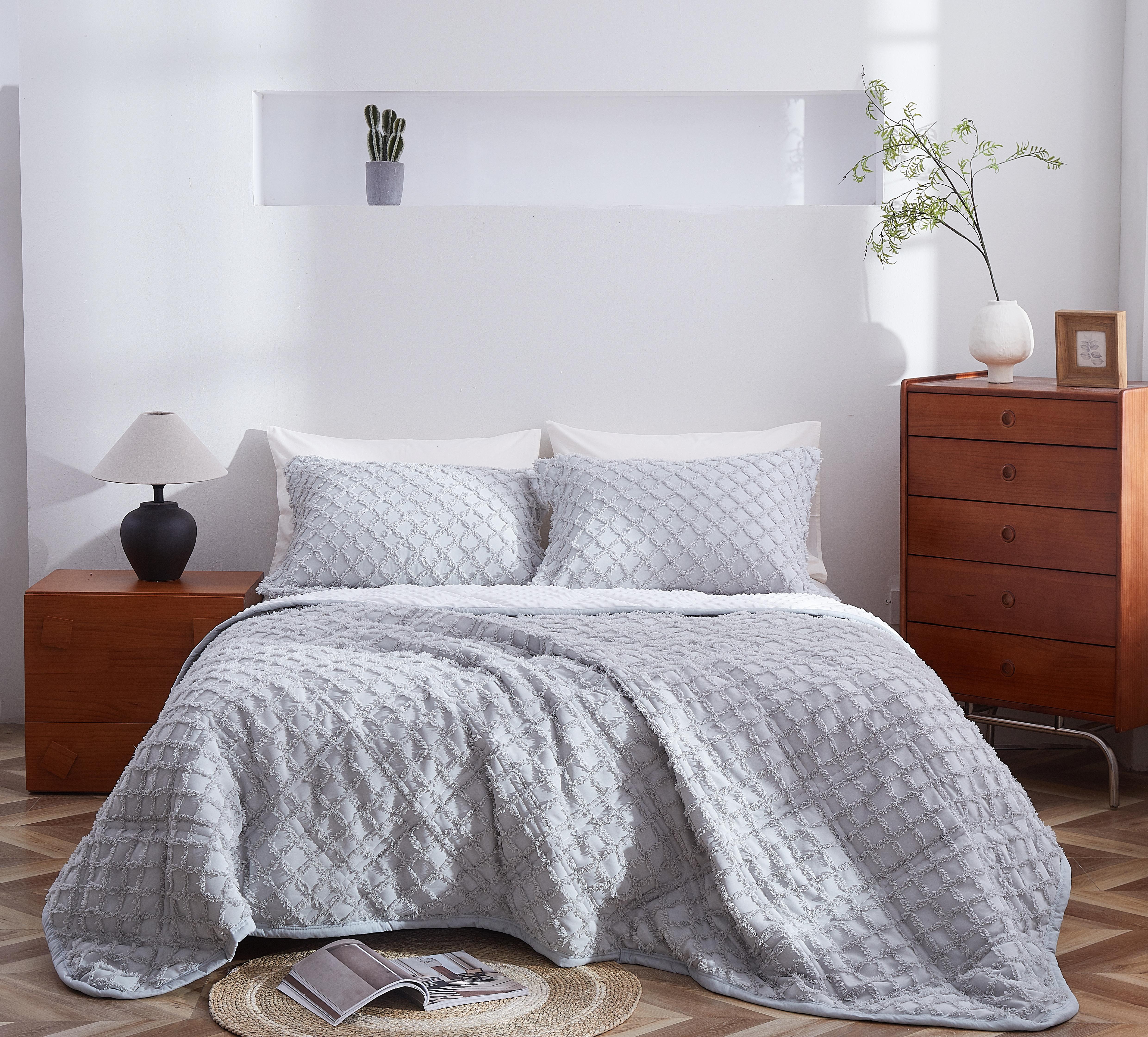 Gray quilted coverlet on a bed in a bedroom with wooden nightstands and decor.