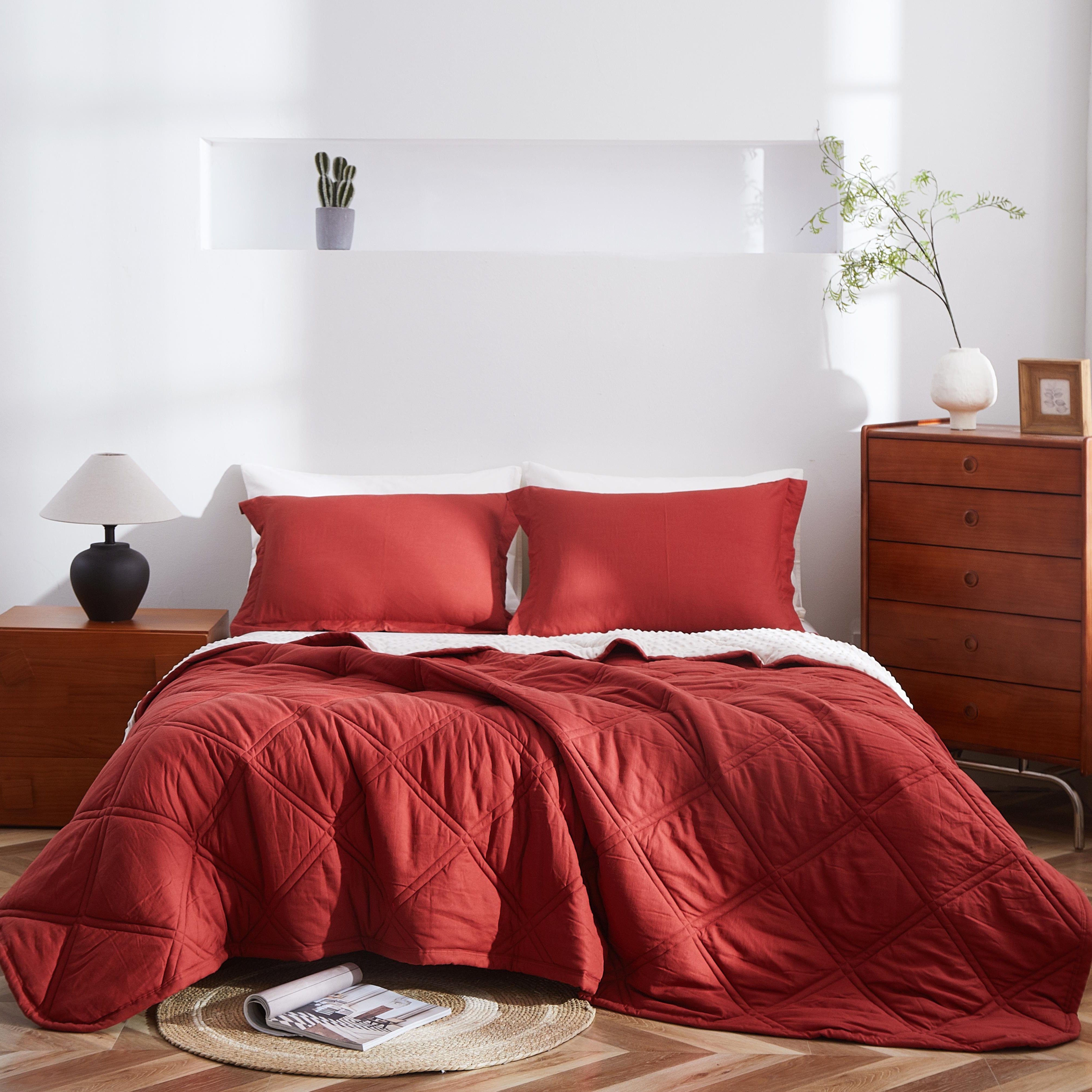 Red quilt and pillows on a bed in a bedroom with wooden furniture and decor.