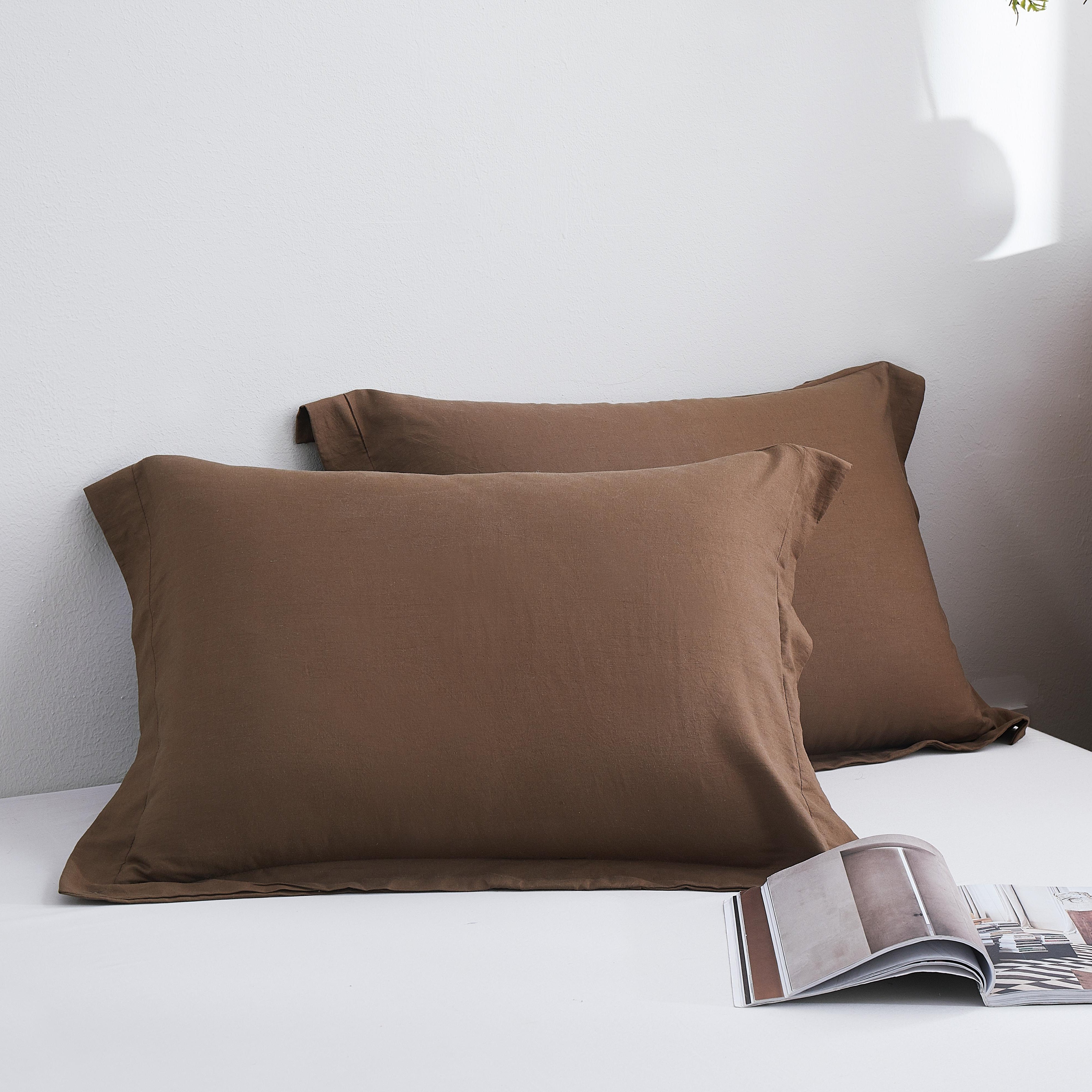 Brown pillows on a bed with a magazine and wooden nightstand in the background