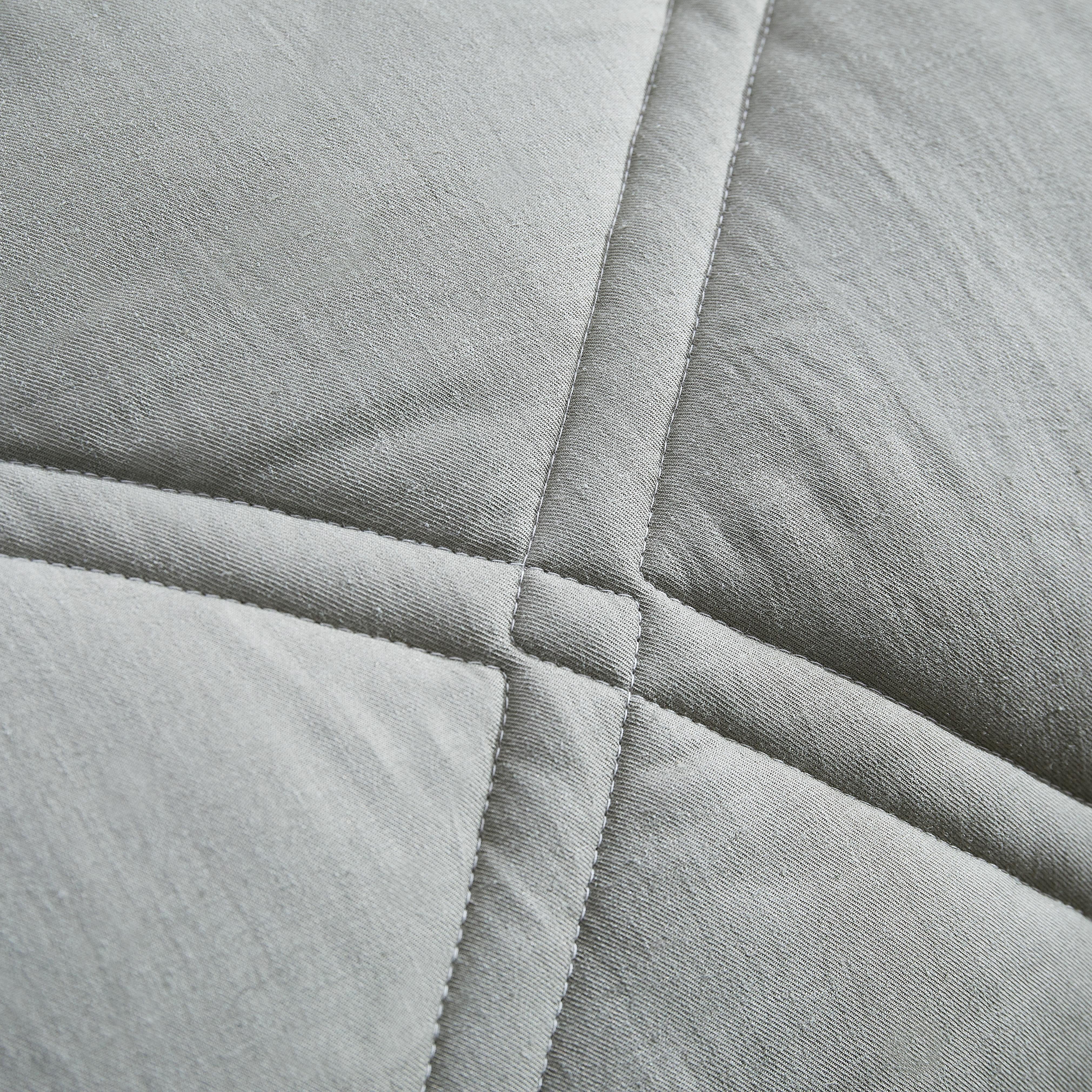 Close-up of a quilted fabric with a diamond pattern in gray tones.