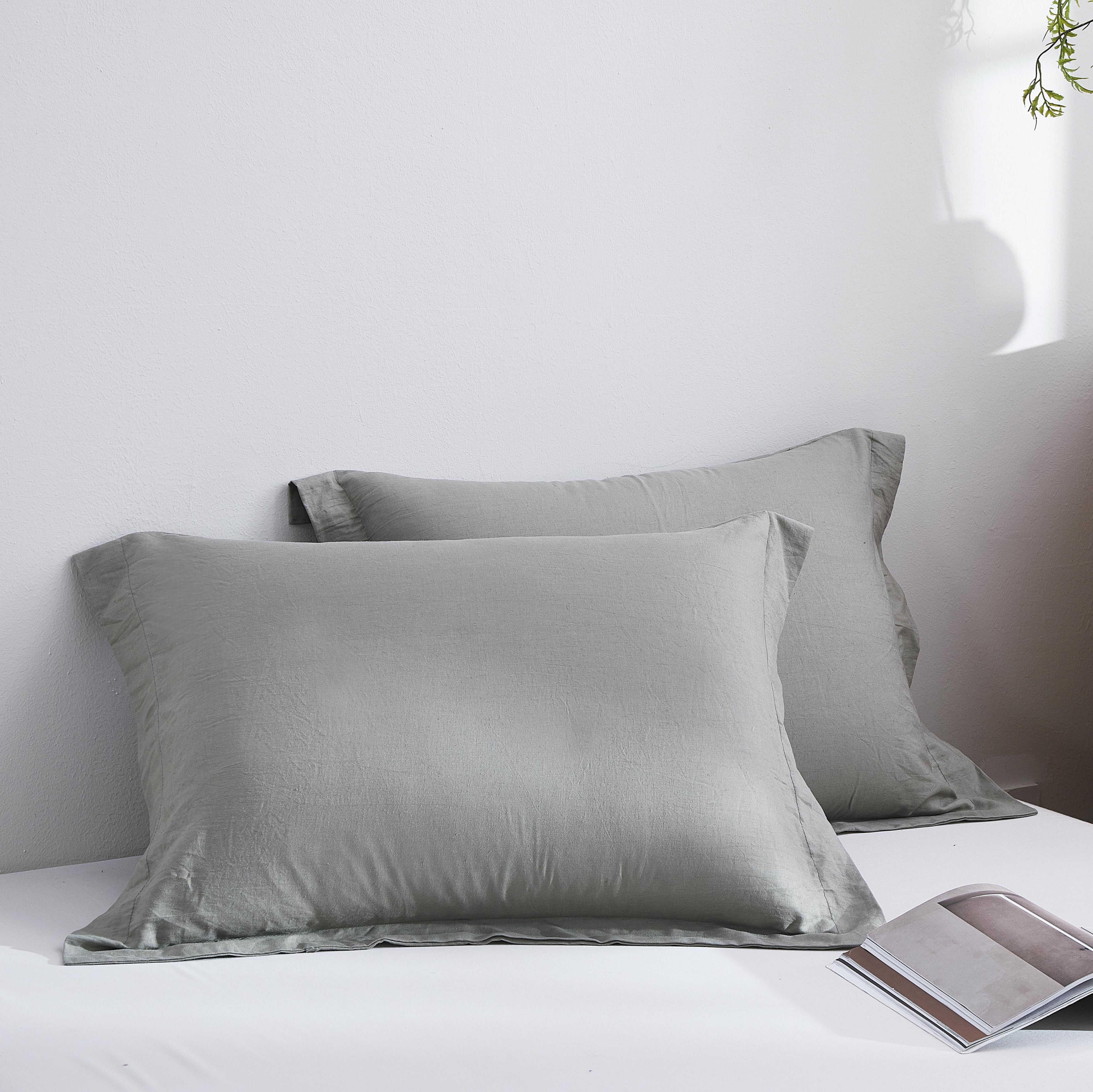 Gray satin pillowcases on a bed with a magazine and wooden nightstand.