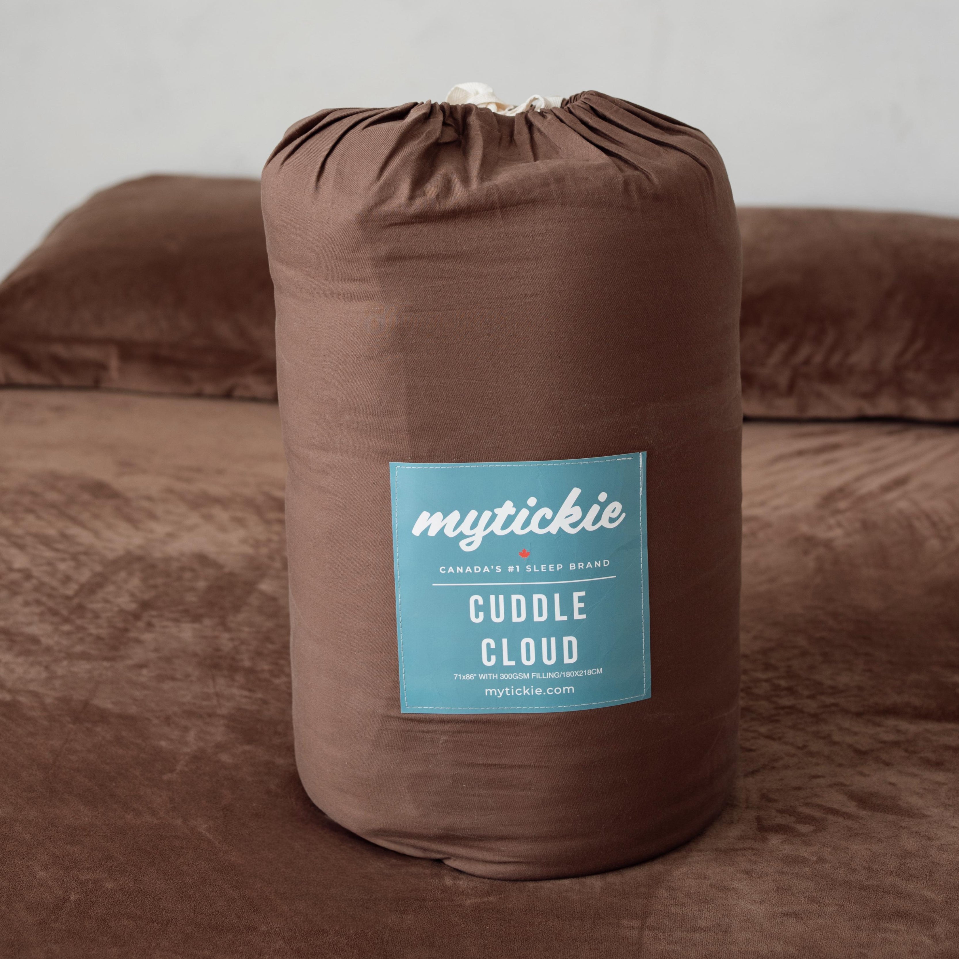 Brown throw blanket in a drawstring bag labeled 'mytickie Cuddle Cloud' on a brown bed