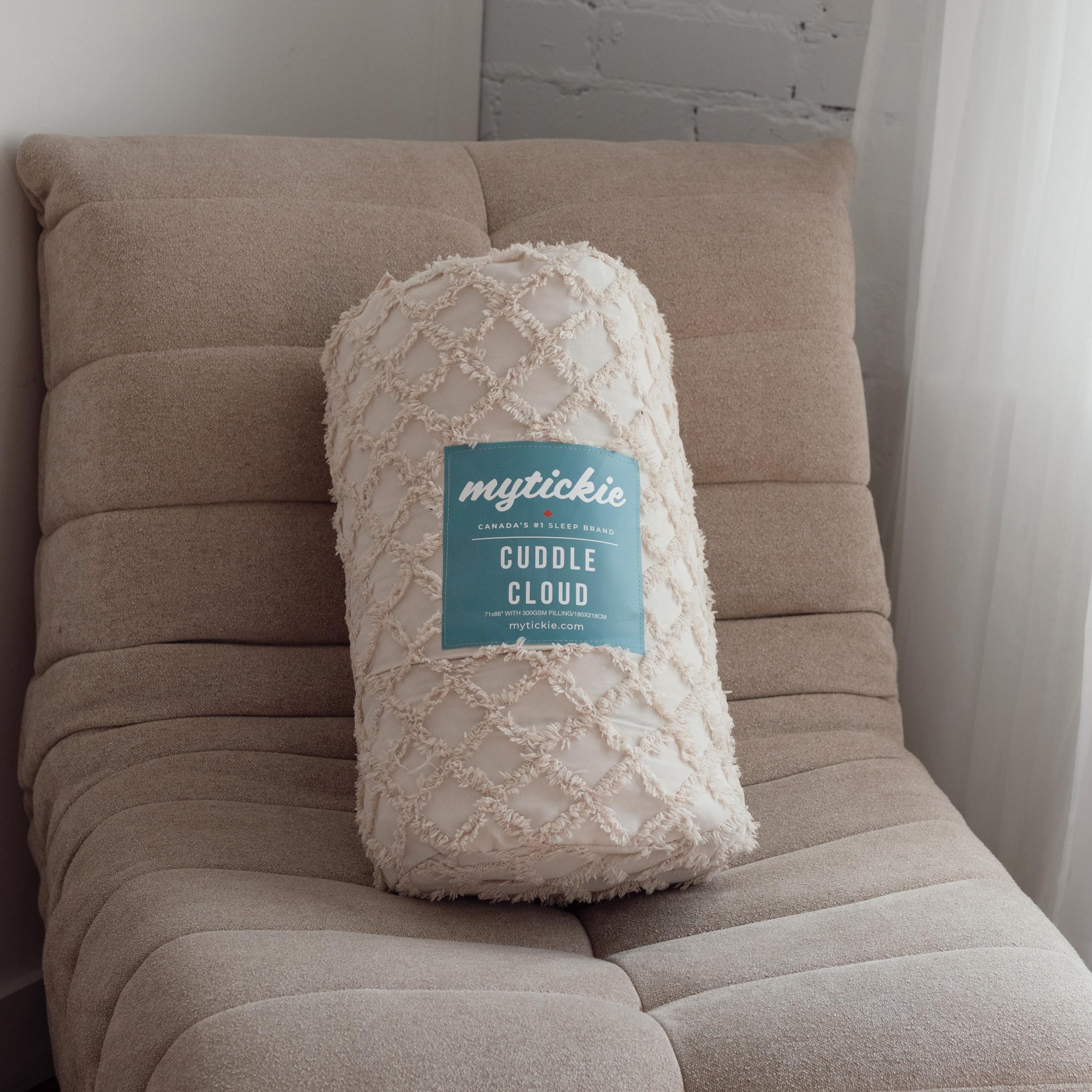 Beige throw blanket labelled 'mytickie' on a chair against a neutral wall.