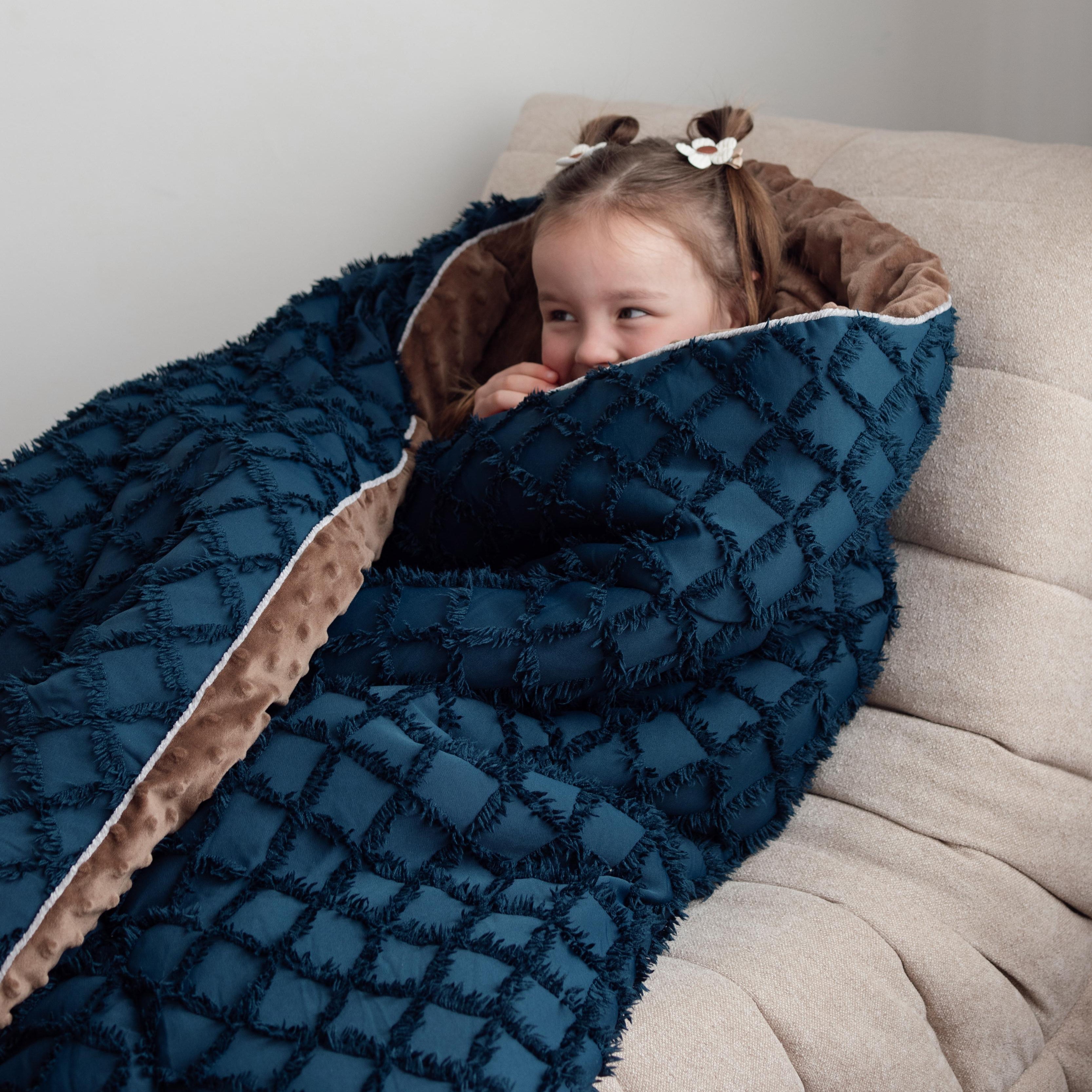 Child wrapped in a blue quilted blanket on a beige couch.