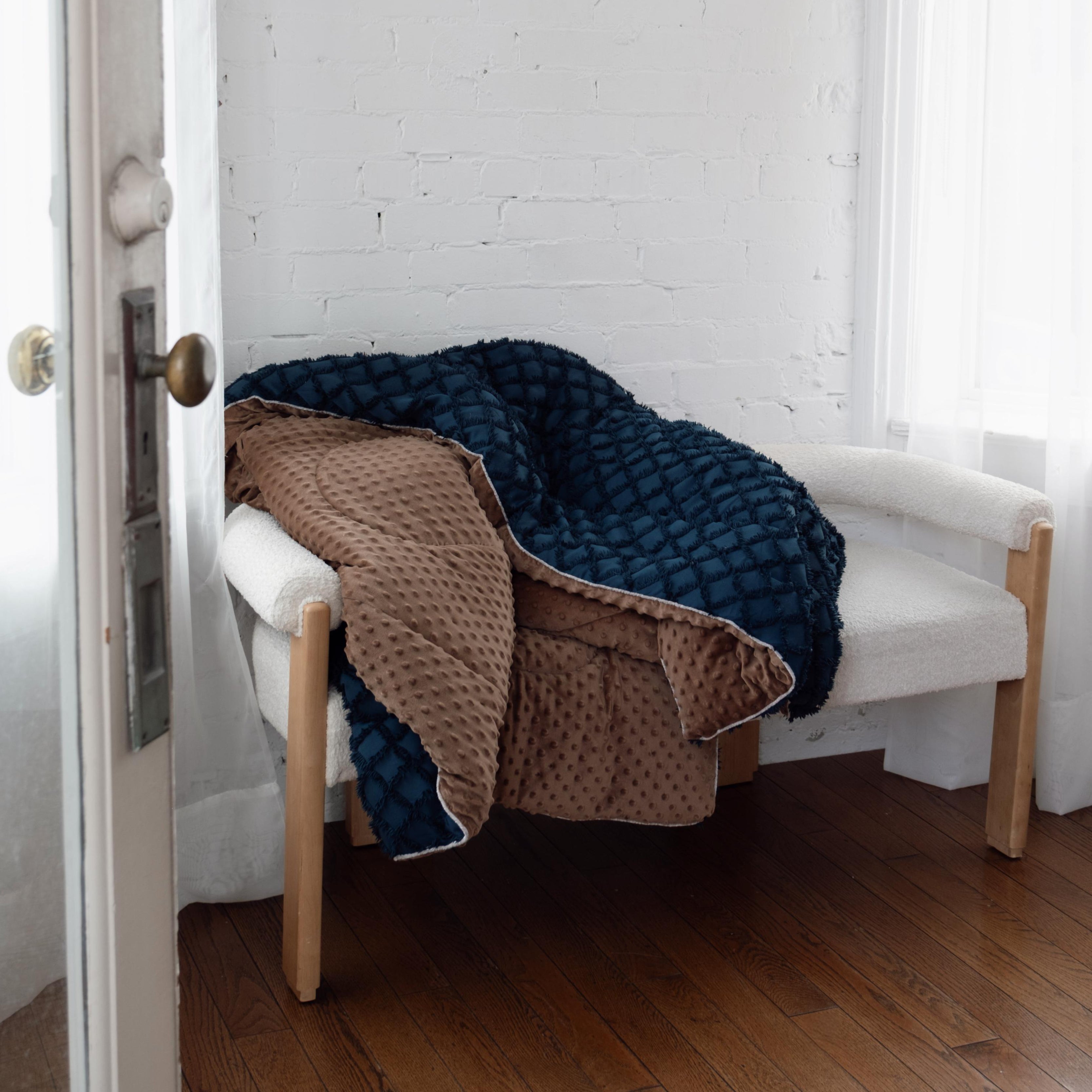 Navy blanket draped over a white bench in a room with wooden flooring and white walls.