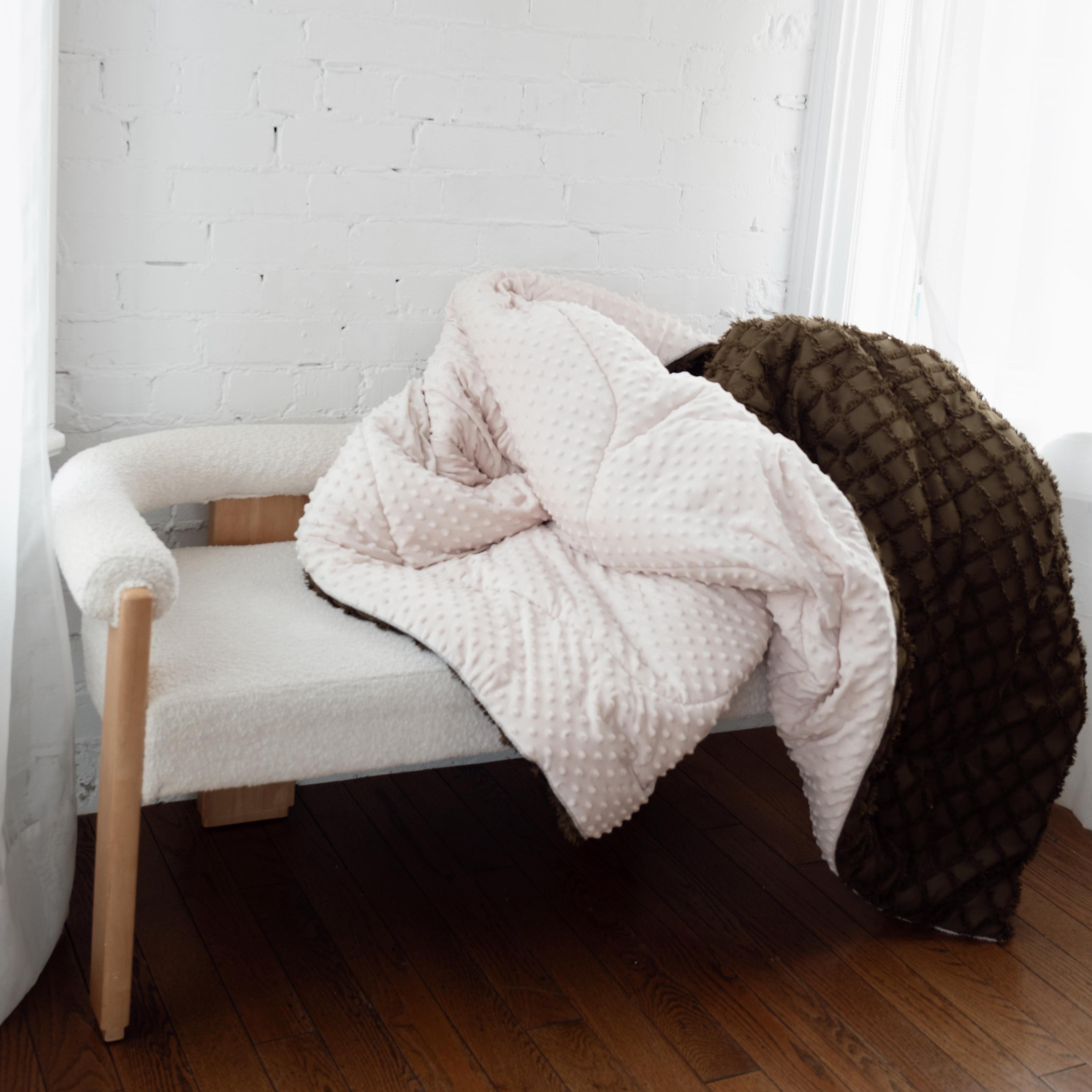 Olive textured throw blanket draped over a white bench against a white wall.