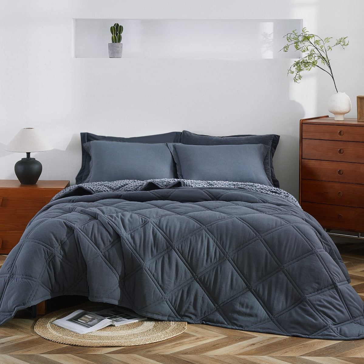 Gray quilted comforter on a bed in a bedroom with wooden nightstands and a lamp.
